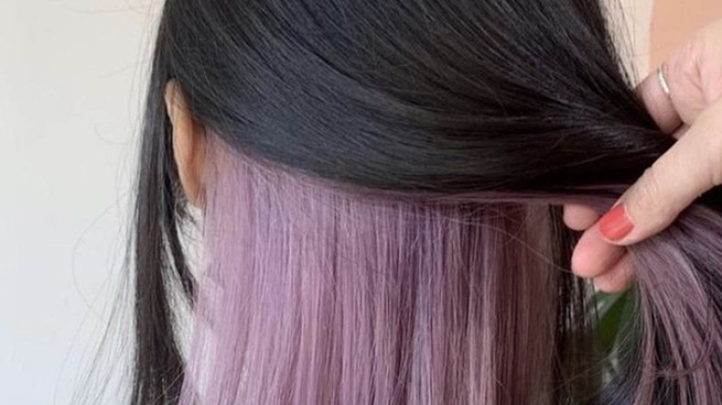 Hand lifting black hair to reveal lavender-colored underlayer showcasing peekaboo hair coloring technique