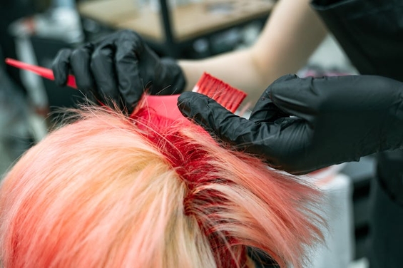 Hairstylist applying red hair dye to blonde hair using brushes creating peekaboo coloring effect