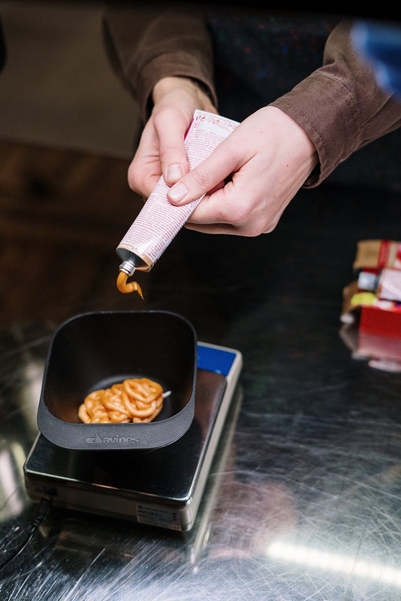 Hands squeezing orange hair dye from a tube into a black mixing bowl for hair coloring preparation
