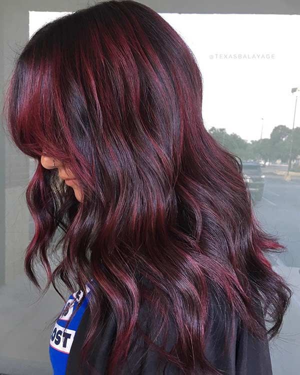 Long wavy black hair with hand painted dark ruby red balayage highlights and side bangs.