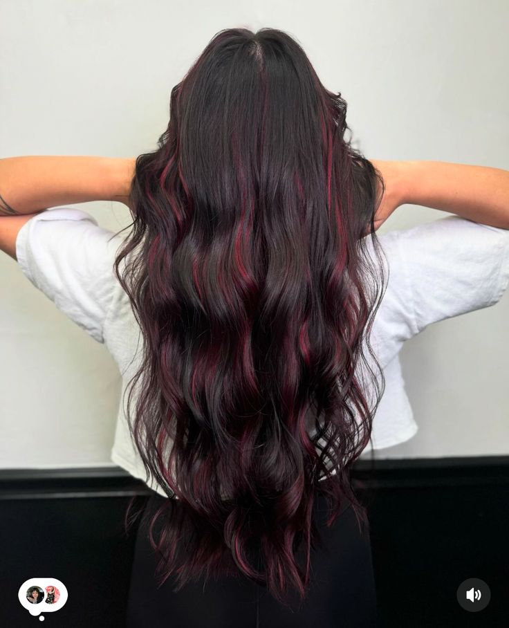 Long layered hair with a classic jet black base and cherry red highlights styled in soft beach waves.