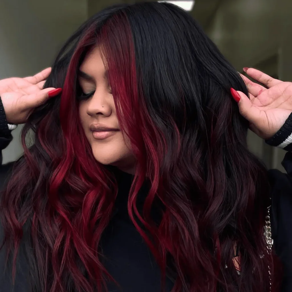 Woman with long wavy black hair featuring vibrant crimson red money piece face framing highlights.