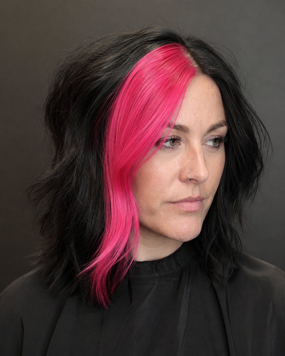 Black shoulder-length hair with one thick vivid-pink skunk stripe